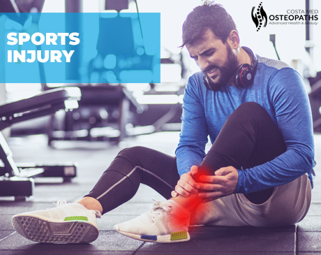 Man sitting on a gym floor clutching his ankle in pain, showing signs of a sports-related injury.