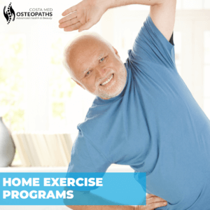 Smiling older man in a blue shirt doing a side stretch at home as part of rehab exercise routine