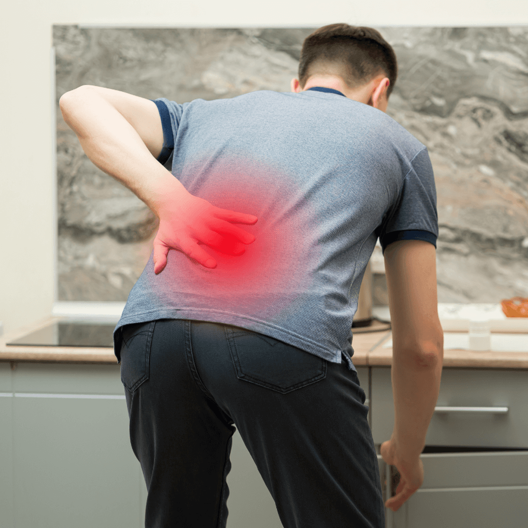Man in kitchen holding lower back in pain, with red glow highlighting the lumbar spine area.